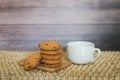 White mug and homemade oatmeal cookies folded in a pile on wooden plate and wooden background