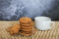 White mug and homemade oatmeal cookies folded in a pile on wooden plate and gray background