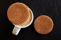 White mug with milky frothy coffee and a round waffle biscuit on