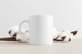 White mug mockup with a cotton branch on a beige table