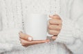 White mug mockup. Girl is holding white 11 oz ceramic cup in hands, wears cozy knitted sweater. Front view, copy space