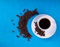 A white mug on a saucer with a black drink is set on a blue background with a number of scattered crescent coffee grains