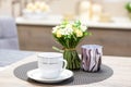 White mug and saucer set. Empty porcelain coffee cup next to decorative flowers and candlestick on wooden table in Royalty Free Stock Photo