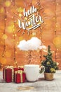 White mug with snowing cloud, present boxes and little Christmas tree with bokeh lights on a wooden table Royalty Free Stock Photo