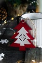A white mug stands on the table, next to a wooden Christmas tree, around a snowflake