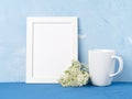 White mug with tea or coffee, frame, flower bouquet on blue table opposite blue concrete wall. Mock up with empty space Royalty Free Stock Photo