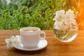 White mug of tea and a vase with jasmine on a wooden table, greens on the background Royalty Free Stock Photo