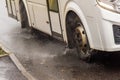 white municipal bus moving on rainy road with water splashes