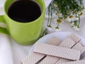 A white napkin with a green cup with coffee, plate of waffles and flowers on it
