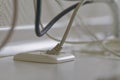 White network cable plugged into a wall socket with tangled wires in background Royalty Free Stock Photo