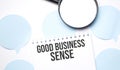 White noteapad and magnifier on blue speech bubles. Text GOOD BUSINESS SENSE. Business concept Royalty Free Stock Photo