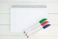 White notebook on metal spiral and three green, red and blue ballpoint pens on wooden table Royalty Free Stock Photo