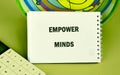 A white notebook open to the phrase Empower Minds is placed next to a calculator and a colorful circular chart