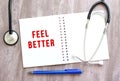 White notebook with red text FEEL BETTER and a stethoscope on a gray wooden table Royalty Free Stock Photo