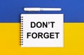A white notebook with the text DO NOT FORGET and a white pen on a blue and yellow background Royalty Free Stock Photo