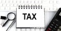 White notebook with text TAX on the white keyboard with calculator,magnifier and pen Royalty Free Stock Photo