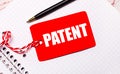On a white notebook there is a black pen and a red price tag on a string with the text PATENT Royalty Free Stock Photo