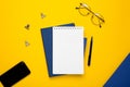 White notepad with blue notebook and pen on yellow background Royalty Free Stock Photo