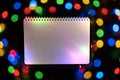 White notepad with defocused colorful bokeh lights on black background, an abstract naturally blurred backdrop Royalty Free Stock Photo