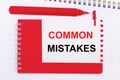 On a white notepad, a red pen, a red notepad and a white sheet of paper with the text COMMON MISTAKES Royalty Free Stock Photo