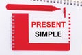 On a white notepad, a red pen, a red notepad and a white sheet of paper with the text PRESENT SIMPLE