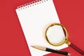 White notepad with a stylish pen, magnifying glass on a red background. Copy space Royalty Free Stock Photo