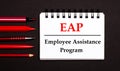 A white notepad with the text EAP Employee Assistance Program, written on a white notepad next to red pens, pencils and markers on