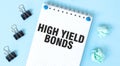 White notepad with text HIGH YELD BONDS and office tools on the blue background Royalty Free Stock Photo