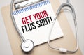 White notepad with the words get your flus shot and a stethoscope on a blue background. Medical concept