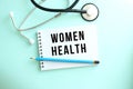 White notepad with the words WOMEN HEALTH and a stethoscope on a blue background.
