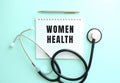 White notepad with the words WOMEN HEALTH and a stethoscope on a blue background.