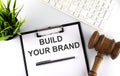 White office desk table with blank sheet , text BUILD YOUR BRAND , keyboard and gavel, top view