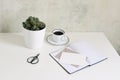 White office desk table mock-up scene with cup of coffee, cactus, open notebook, blank greeting card, envelope and