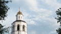 White old christian church, chapel with golden dome and cross against cloudy sky framed by trees, outdoor exterior. Royalty Free Stock Photo