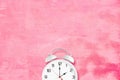 White alarm clock with twin bells and ringer on pink texture as background