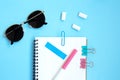 White open notebook with blue elements, gum and sunglasses on a light blue background