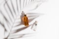 White, orange and black serum bottles on white background. Trending shadow from a palm branch. Cosmetic mockup. Place to