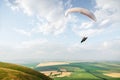 A white-orange paraglider flies over the mountainous terrain