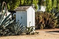 White Outhouse with Cactus Plants in Garden