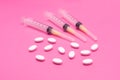 White oval tablets are scattered along with three disposable syringes on a pink background. Macro copy space Royalty Free Stock Photo