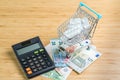 White package medicine or pills in miniature shopping cart or trolley with calculator on pile of Euro banknotes money on wood Royalty Free Stock Photo