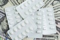 White package of pills on pile of US dollar banknotes money, medical, drug and health care industry concept, cost that patient