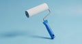 A White Paint Roller with a Blue Handle Suspended Against a Solid Light Blue Background roller brush Royalty Free Stock Photo