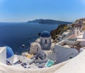White painted houses and blue domed churches in the village of Oia, Santorini with Thirasia island in the background Royalty Free Stock Photo