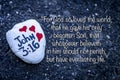 A white painted rock and with three red hearts that has the Bible Verse John 3:16 in black paint