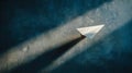 White paper airplane casting a long shadow on textured blue wall illuminated by a diagonal beam of soft natural light creating a Royalty Free Stock Photo