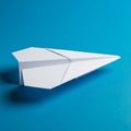 White paper airplane on a solid blue background. The airplane is folded into a classic triangular Royalty Free Stock Photo