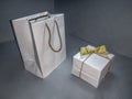 White paper bag with yellow handles and a gift box with a gold bow. Mockup cardboard box and holiday packaging for overlaying a