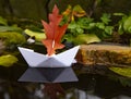 A white paper boat with a red sail on the dark water in a small pond. Royalty Free Stock Photo