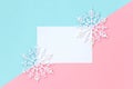 White paper card decorated with snowflakes on pink and light blue background. Royalty Free Stock Photo